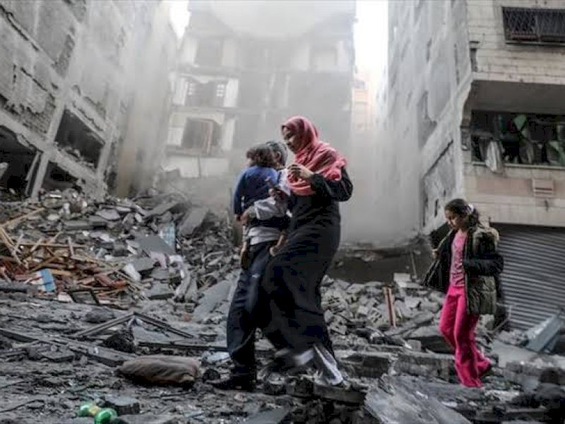 Warga Palestina berjalan di antara reruntuhan yang digempur Israel. (int) 