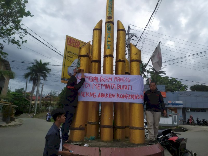 Demonstran membentangkan spanduk protes terhadap mobil mewah Bupati Enrekang. 