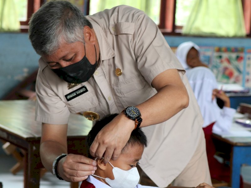 Bupati Pinrang Irwan Hamid mengenakan masker kepada salah seorang siswa. (Ist)